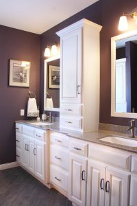 Painted white bathroom vanity with linen cabinet dividing the two sinks