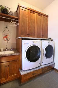 Laundry room with washer and dryer sitting on a pedestal and custom black walnut cabinets